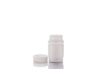 A jar of pills and an open lid stands on a mirror surface on a white background in the middle.