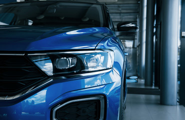 Front part of brand new modern blue car. Parked at showroom. Reflection in the headlights