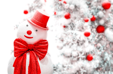 White snowman with red bowtie and hat on blurred decorating christmas tree