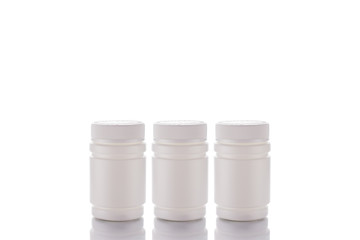 Three jars of pills and a closed lid stand on a mirror surface on a white background in the middle.