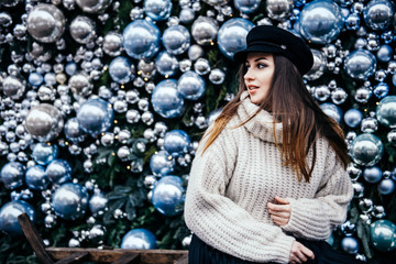  young woman in warm oversize sweater posing near christmas decorations outdoor