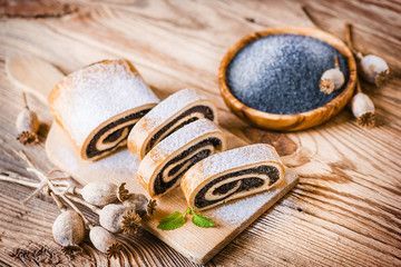 Fresh beautiful poppy roll cakes or strudel on old table. Poppies heads and seed in background