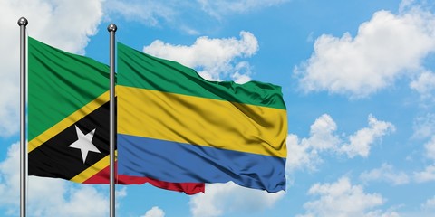 Saint Kitts And Nevis and Gabon flag waving in the wind against white cloudy blue sky together....