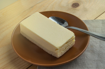 Appetizing piece of vanilla cheesecake new York on a brown ceramic plate with a small spoon, wooden...