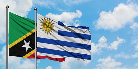 Saint Kitts And Nevis and Uruguay flag waving in the wind against white cloudy blue sky together....