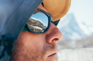 Portrait shot of high altitude unshaven happy mountain hiker in baseball cap and hood with snow...