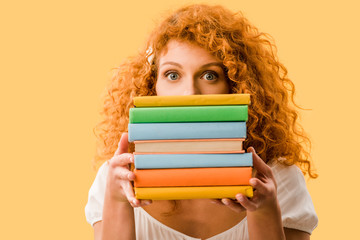 female redhead student holding books isolated on yellow