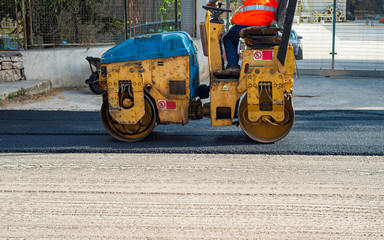 Worker leads the vibrating road roller to compact the asphalt laid out for the construction of a road