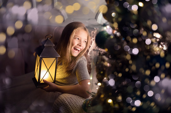 Portrait of a cheerful cute girl near a Christmas tree with a lantern. New Year holidays.