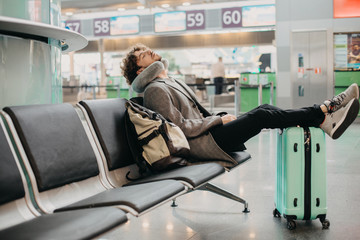 Young businessman sleep alone in waiting room. Sit in airport or train station. Hold legs on...