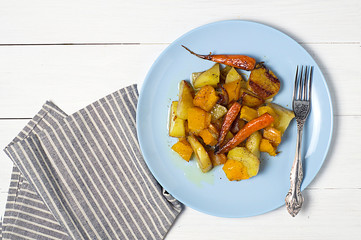 Warm autumn salad with pumpkin, potatoes, carrots on a platter on a white wooden background.