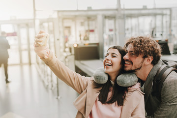 Picture of young man and woman posing for selfie together. Woman hold phone in hand. People smile. Waiting for flight. Going to travel abroad. Small trip or vacation.