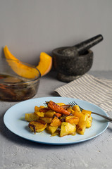 Warm autumn salad with pumpkin, potatoes, carrots on a platter on a gray concrete background.