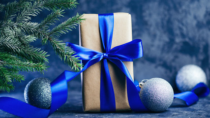 Beautiful gift box with blue ribbon, tree branches and balls close up