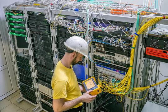 The engineer in a white helmet measures the level of the optical signal in the server room of the data center. A technician diagnoses a problem area in a telecommunication network.