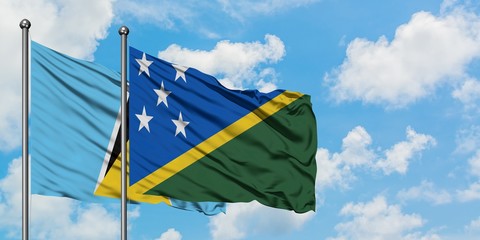 Saint Lucia and Solomon Islands flag waving in the wind against white cloudy blue sky together....