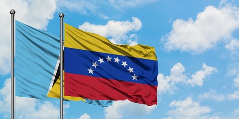 Saint Lucia and Venezuela flag waving in the wind against white cloudy blue sky together. Diplomacy...
