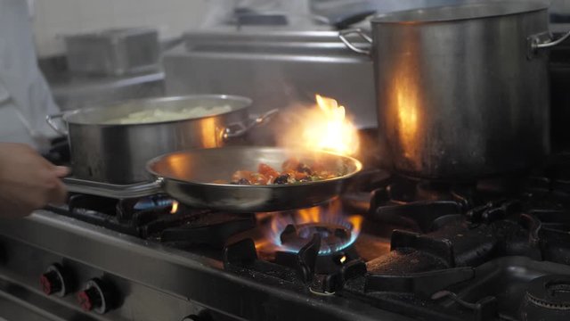 Slow motion closeup of a chef preparing flambe style dish on a frying pan.