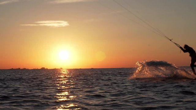 Slow motion of kitesurfer silhouette doing a trick in sunset