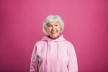 Happy cheerful positive old woman smiling wide and look straight on camera. Stand straight. Modern...
