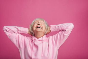 Emotional happy old woman laughing out loud alone. Hold hands behind head. Look up with eyes...