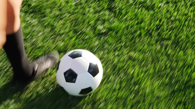 Close up on the cleats of a soccer player running with a football dribbling up the grass field to score a goal and win the game.