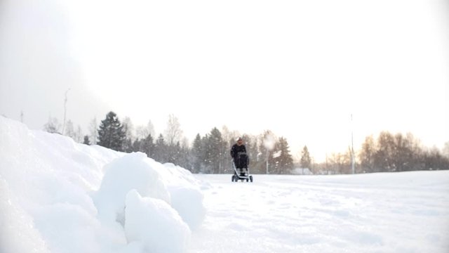 Static slow motion shot of father walking with baby stroller in snowy winter storm