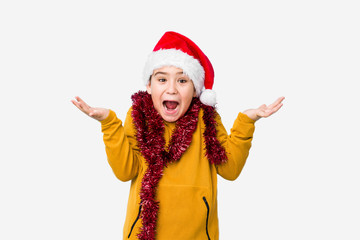 Little boy celebrating christmas day wearing a santa hat isolated celebrating a victory or success, he is surprised and shocked.