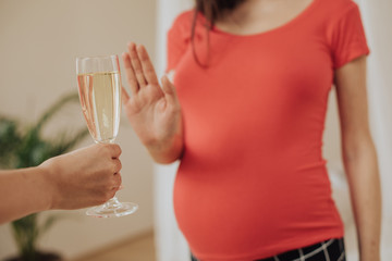 Cut view of pregnant woman showing stop sign to hand that holds glass of champaign in hand. No...