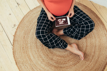 Cut view of barefeet young woman sitting on floor alone and hold ultrasound picture of her future...