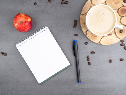 Morning workplace as cup of coffee, coffee beans, apple and notepad, pen for notes. Minimalism concept