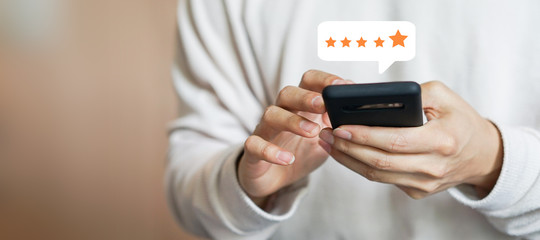 close up on customer man hand pressing on smartphone screen with gold five star rating feedback icon and press level three rank (good) for give score point to review the service business concept	