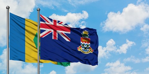 Saint Vincent And The Grenadines and Cayman Islands flag waving in the wind against white cloudy...