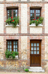 Fototapeta na wymiar typical Normandy architecture house front with stone and brick facade and colorful flowerpots