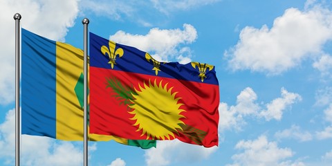 Saint Vincent And The Grenadines and Guadeloupe flag waving in the wind against white cloudy blue...