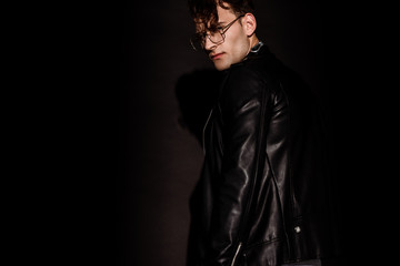 Fototapeta na wymiar trendy man in glasses and leather jacket standing on black