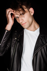 stylish young man in leather jacket touching hair isolated on black