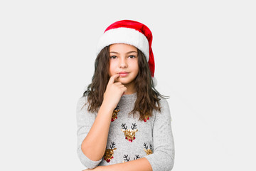 Little girl celebrating christmas day looking sideways with doubtful and skeptical expression.