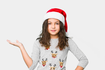 Little girl celebrating christmas day showing a copy space on a palm and holding another hand on waist.