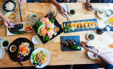 A set of sushi on a wooden table in a Japanese restaurant.Fresh salmon sliced for sushi menu.Party of friends or family eating sushi using bamboo sticks.