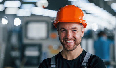 Smiling and happy employee. Portrait of industrial worker indoors in factory. Young technician with...