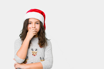 Little girl celebrating christmas day thoughtful looking to a copy space covering mouth with hand.