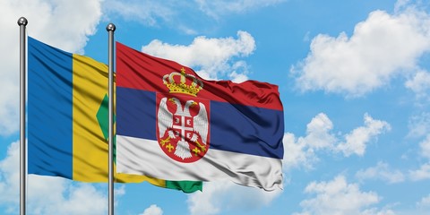 Saint Vincent And The Grenadines and Serbia flag waving in the wind against white cloudy blue sky...