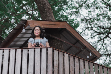 Fototapeta premium Beautiful Asian woman with film camera standing on wooden cabin which built on tree