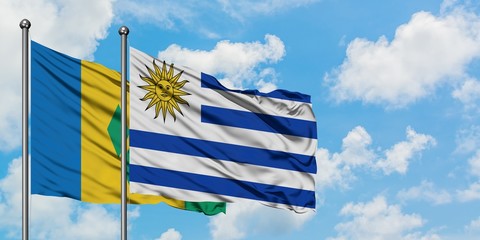 Saint Vincent And The Grenadines and Uruguay flag waving in the wind against white cloudy blue sky...