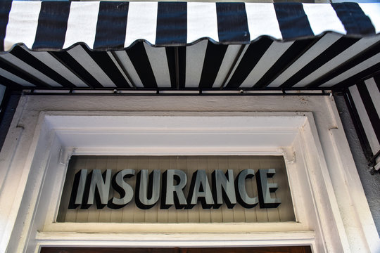 A Vintage Sign In Silver Type On A Transom Window Reads INSURANCE, While A Bold Black And White Awning Flutters Overhead.