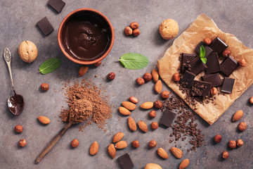 Chocolate, cocoa powder, a variety of nuts and mint leaves on a dark brown rustic background. View...