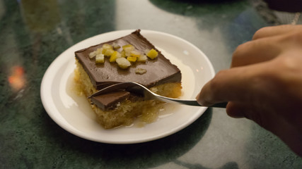 Dude taking with a fork orange dessert with syrup in restaurant. Homemade cake with chocolate on a plate.