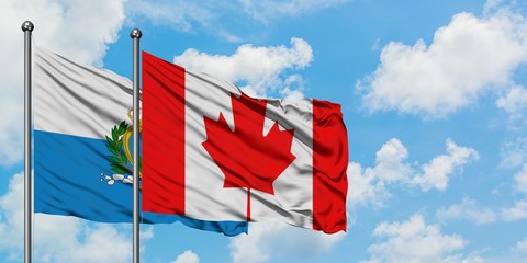 San Marino and Canada flag waving in the wind against white cloudy blue sky together. Diplomacy...