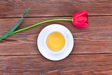 Cup of green tea with red tulip flower on a wooden background. Top view.